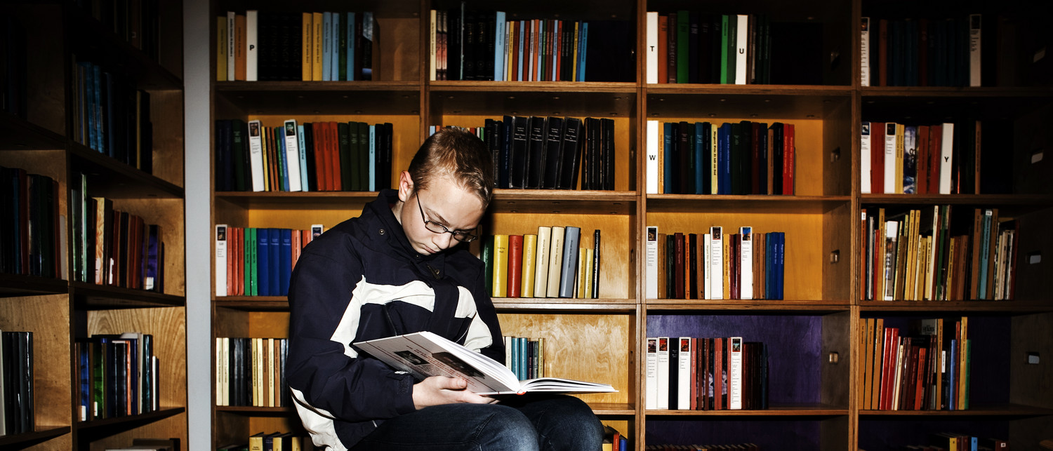 Dreng læser foran en stor bogreol